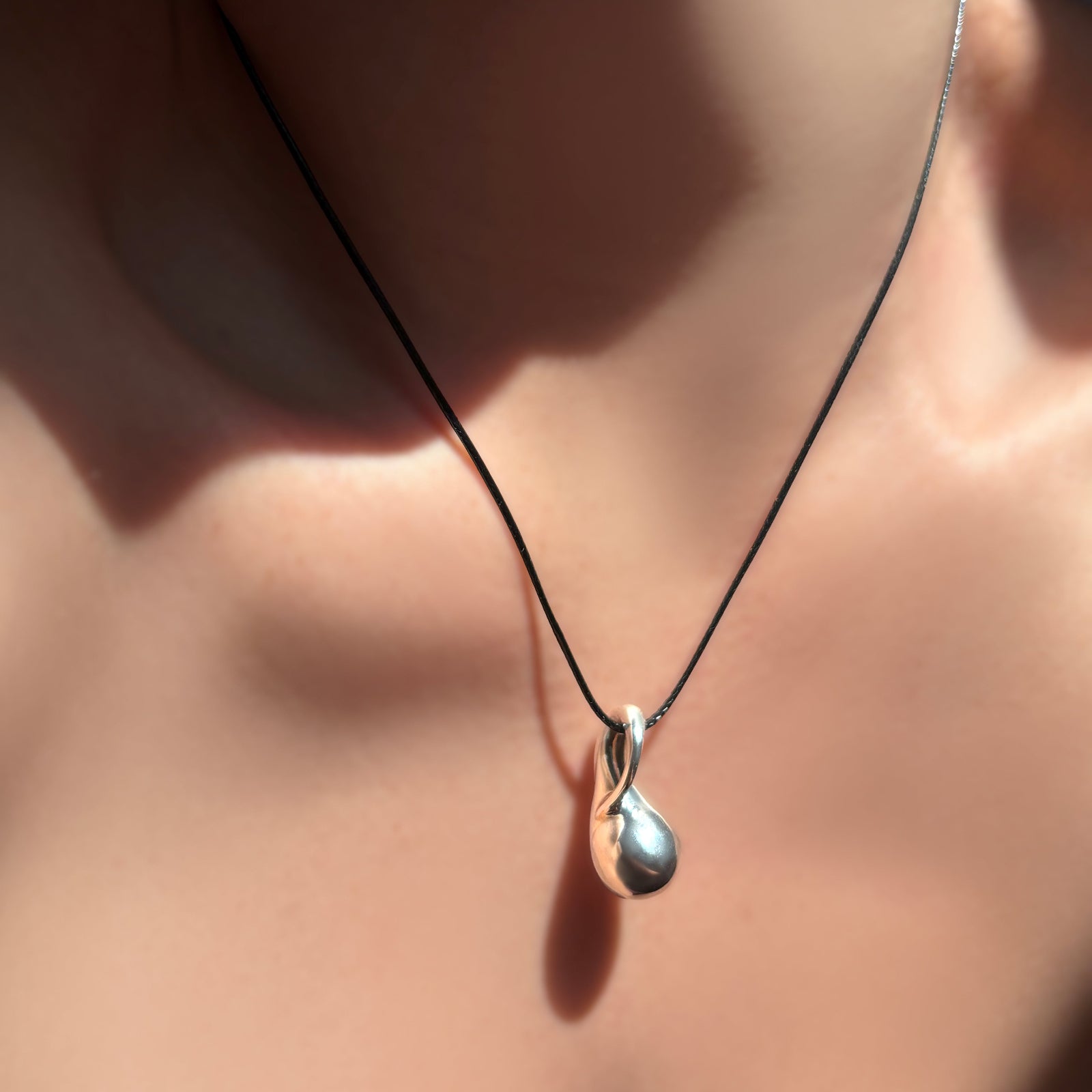 Molten sterling silver drop charm on a black cord necklace.