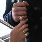 Two hands clad in AMANDA PEARL sterling silver molten rings holding the pole in a new york city subway car.