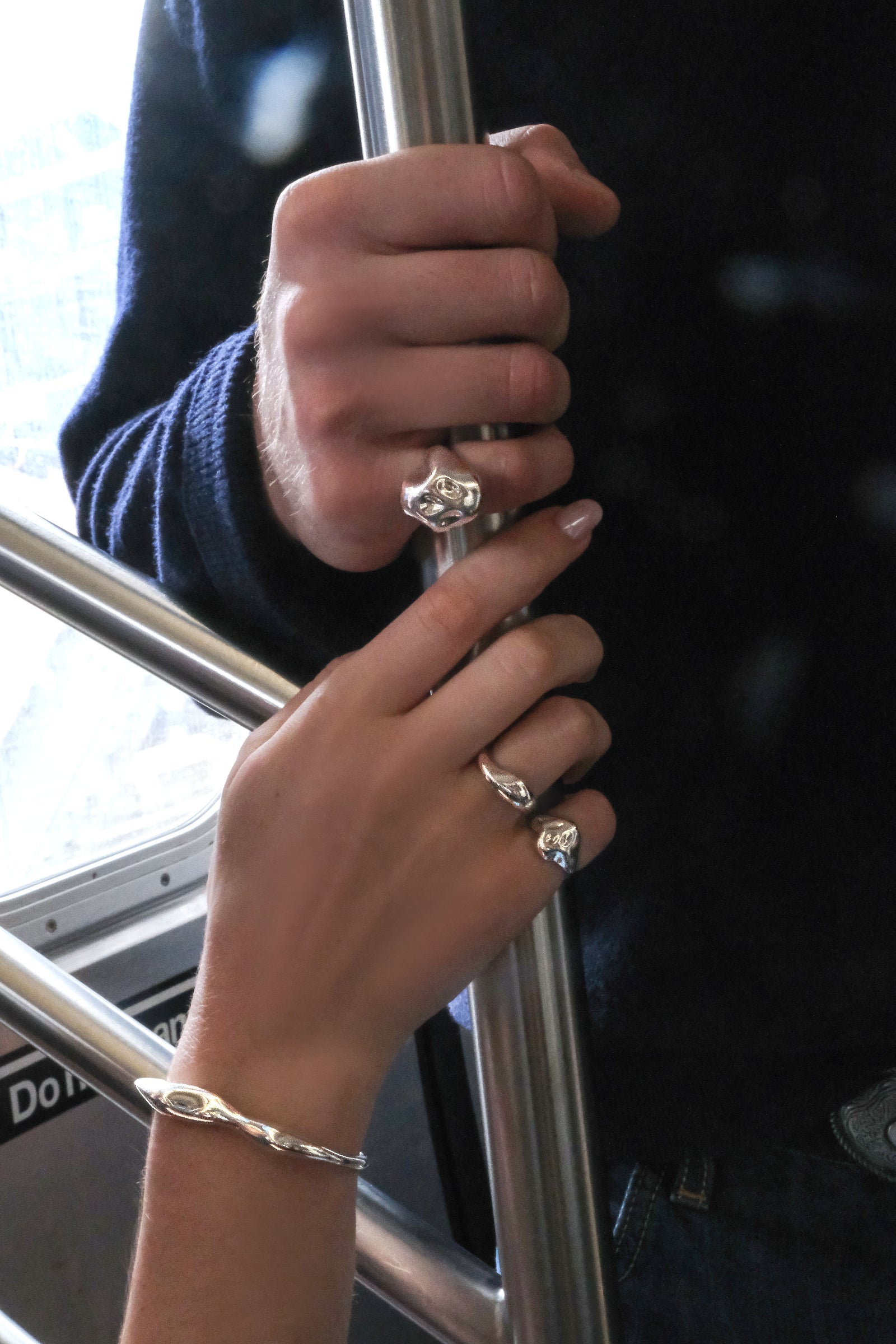 A man and a woman's hand grip chrome subway car pole, as they wear reflective sterling silver AMANDA PEARL jewelry. They are in New York City. 
