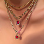 Tibet chain, drop link chain with molten solitaire charm with ruby, and irregular cable chain with molten knot charm with ruby and a ruby charm lock hanging on a model's neck.