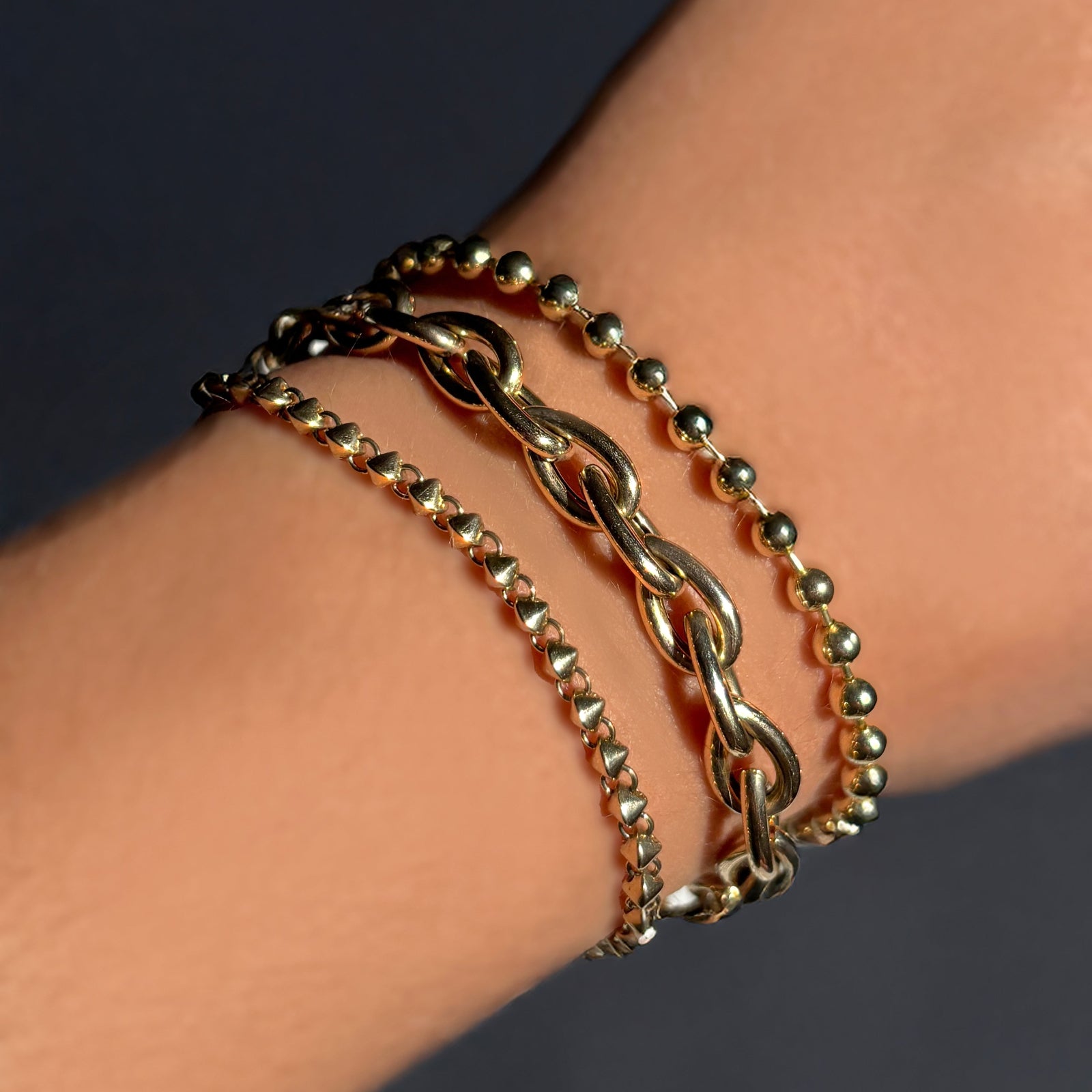 14k gold Tibet Chain Bracelet layered with Drop Link Chain Bracelet and 4mm Bead Chain Bracelet on a model's wrist.