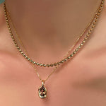 Tibet chain layered over a diamond cut bead chain with molten knot charm with tourmaline on a model's neck.