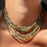 6 tide pool opal necklaces layered on the neck against bare skin in sunlight.