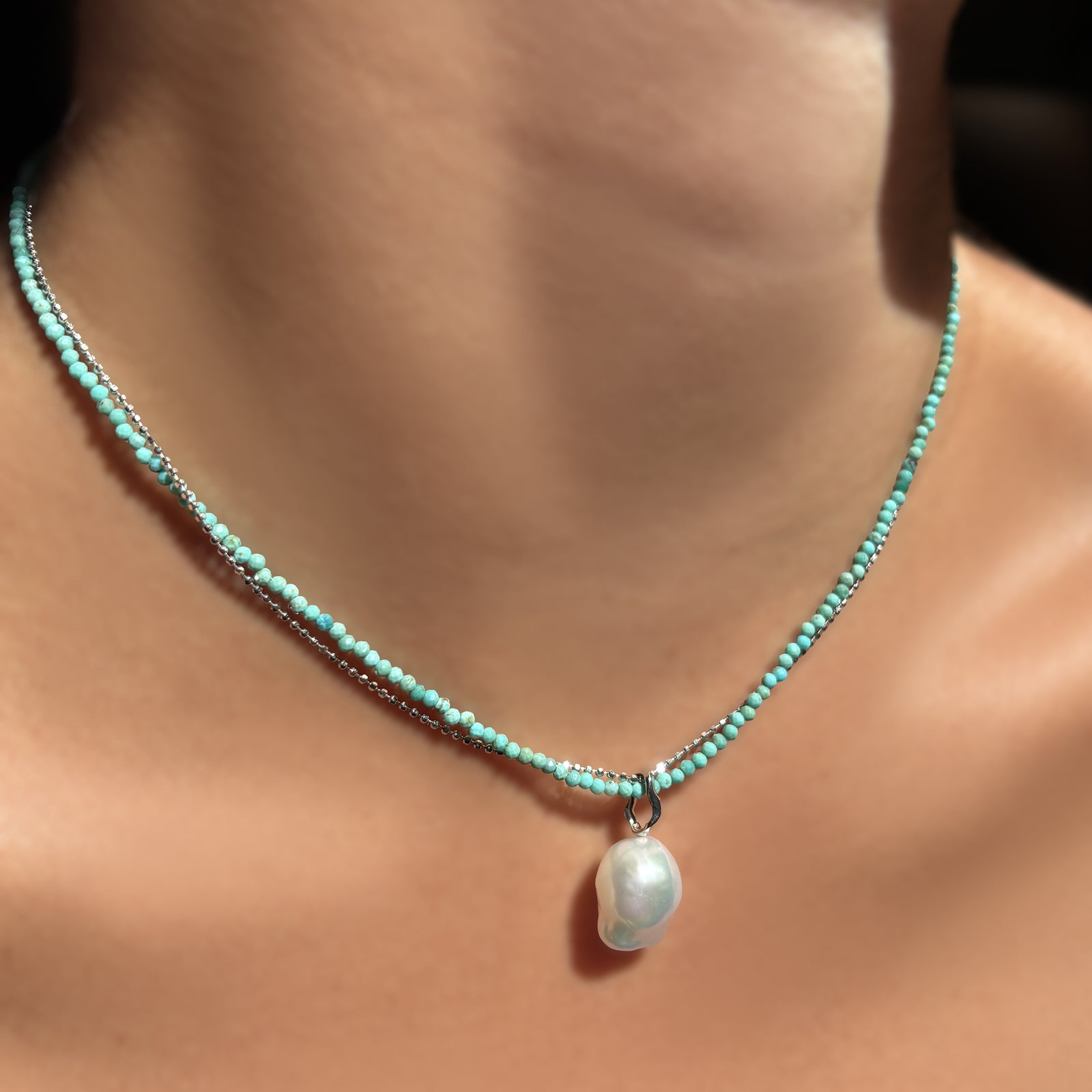 A slim gemstone necklace in turquoise wrapped with a diamond cut bead chain in white gold, with a mini baroque pearl charm with white gold ripple bale hanging on the neck.