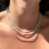 An stack of AMANDA PEARL White Zircon slim gemstone necklaces on a model's neck.
