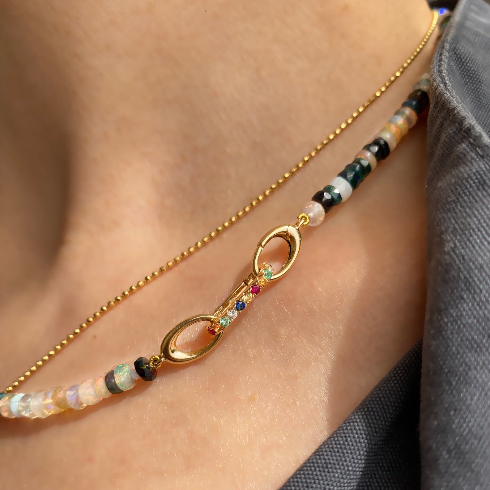 14k yellow gold small oval locking charm with rainbow colored stones. Styled on a neck locked into oval clasps of a beaded necklace.