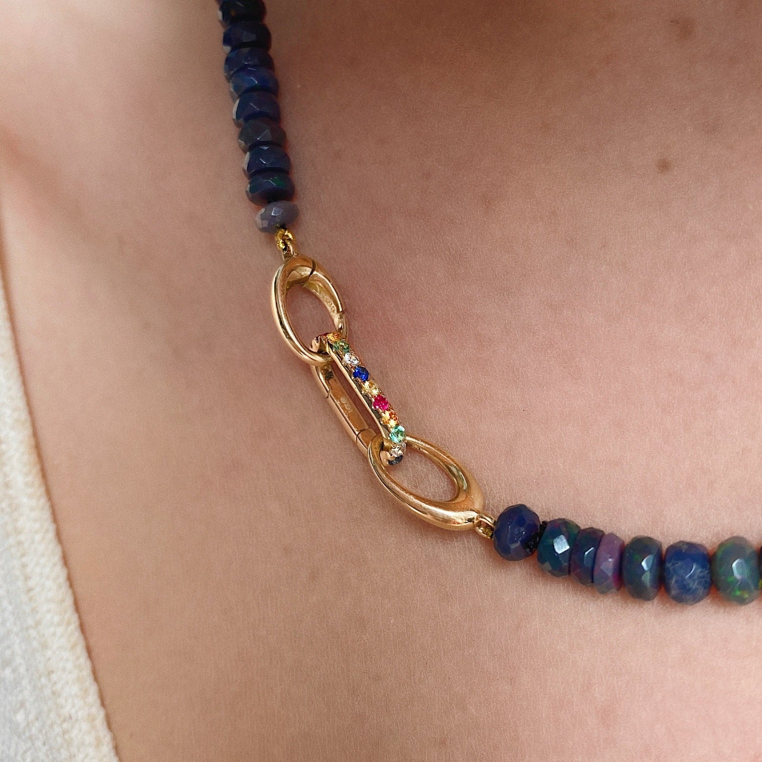 14k yellow gold small oval locking charm with rainbow colored stones. Styled on a neck locked into oval clasps of a beaded necklace.