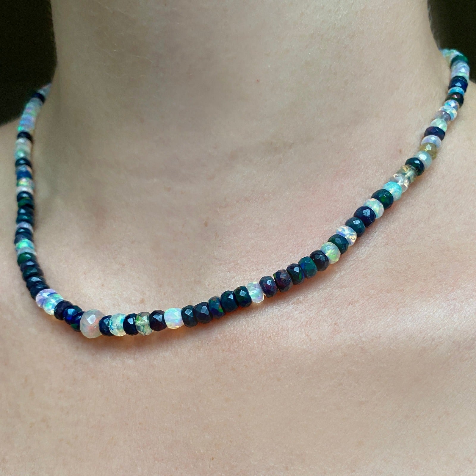 Shimmering beaded necklace made of faceted opals in shades of fiery pastels, grey, teal, and black on a gold linking ovals clasp.
