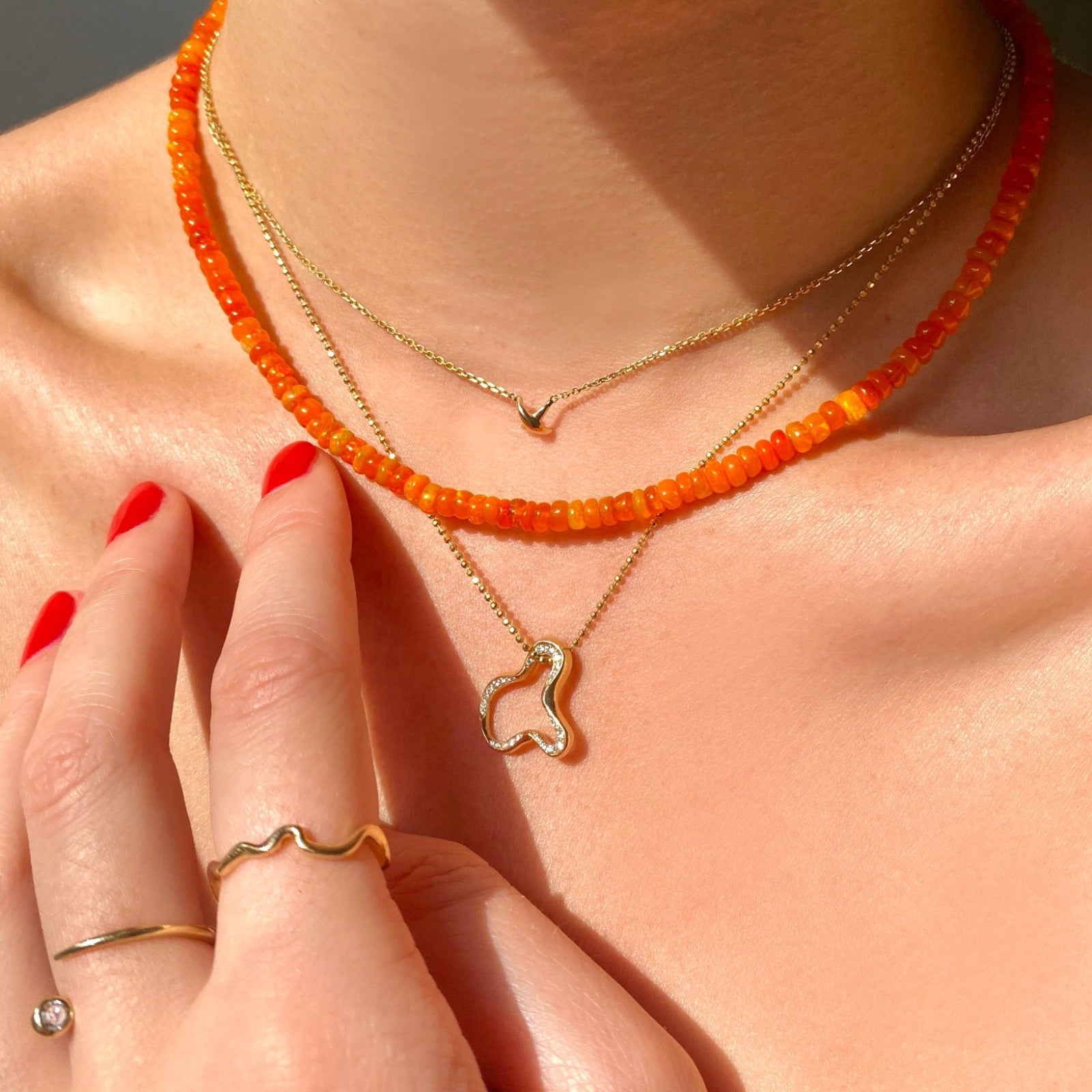 Shimmering beaded necklace made of smooth opal rondels in shades of orange on a slim gold lobster clasp. Styled on a neck layered with the ripple charm and stitch necklace.